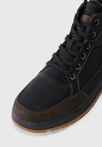 Zapatillas altas en negro y marrón con cuero texturizado, acentos de ante y costuras en contraste. Suela de goma con un dibujo en relieve.