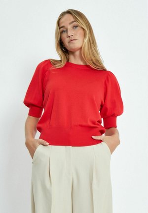 Jersey rojo de punto con mangas cortas abullonadas y dobladillo acanalado, combinado con pantalones de talle alto en beige claro. Textura suave y diseño ajustado.