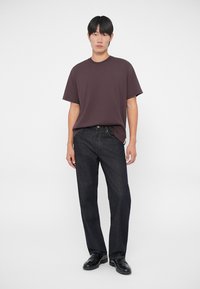 Temno rjava majica s kratkimi rokavi, temno modri jeans ravnega kroja in črne čevlje. Preprost dizajn z udobnim prileganjem in gladko teksturo.