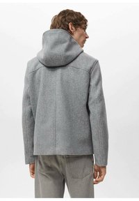 Szara wełniana kurtka z dopasowanym kapturem, czystymi liniami i detalami szwów, zestawiona z jasnoszarymi spodniami. Tekstura wydaje się miękka i uporządkowana.