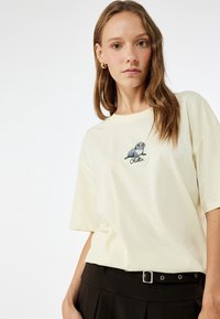 Kerman puuvillapaita, jossa on rento istuvuus, lyhyet hihat ja etupuolella kirjailtu sinetti, jonka alla lukee "Chillin".