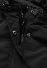 Veste noire en tissu durable, avec des boutons métalliques et une fermeture éclair. À l'intérieur, un tissu doux et contrasté.