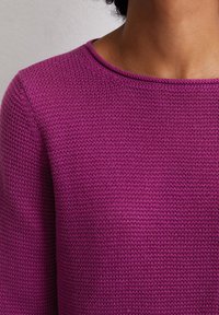 Magenta Pullover mit strukturiertem Strickmuster, runder Ausschnitt und langen Ärmeln. Nahaufnahme, die sich auf das Detail des Stoffs und die Farbe konzentriert.