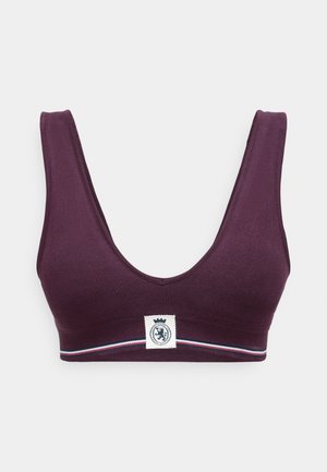 V-veida purpura sporta krūšturis, izgatavots no ribota auduma, ar logotipa ieliktni un horizontālu joslu sarkanā un baltā krāsā gar jostu.