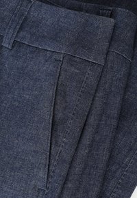 Pantalones vaqueros en un índigo profundo, con una textura suave, frente plano, trabillas para el cinturón y un costurón preciso a lo largo de las costuras.