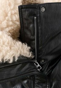 Giacca in pelle nera con una morbida fodera in shearling beige. Include una chiusura con zip argentata e un dettaglio con bottone a pressione sul colletto.