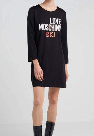 Personne portant une robe noire à manches longues avec "LOVE MOSCHINO" barré et "SKI" écrit en dessous en lettres rouges.