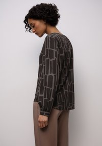 Maglia a maniche lunghe grigio scuro con motivo geometrico astratto grigio chiaro, con scollo rotondo e maniche arricciate, abbinata a pantaloni beige.