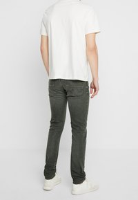 Vit bomullst-shirt, bakifrån, tillsammans med mörkgröna jeans och vita sneakers, som framhäver enkel design och avslappnad stil.