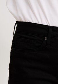 Svarta denimjeans har en figurnära design med en synlig ficka och sömdetaljer. Materialet verkar slitstarkt med en slät textur.