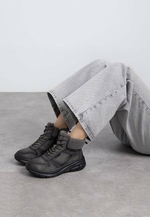 Zapatillas altas negras con suelas de goma texturizadas y un acogedor cuello de forro polar gris, combinadas con jeans de pierna ancha gris claro.