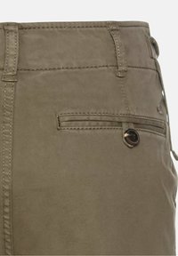 Gros plan sur la poche arrière d’un pantalon kaki avec une fente horizontale et une fermeture par bouton foncé du côté droit.