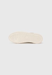 Sneaker sole in beige rubber, featuring a textured tread pattern with grooves and a circular detailing near the center.