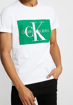 Weißes Baumwoll-T-Shirt mit einem grünen rechteckigen Grafikdesign, das "CALVIN KLEIN JEANS" und ein großes "CK" in weißer Schrift zeigt.