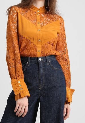 Orange blonderet skjorte med solidt stof i chevron-design, knaplukning foran og flæsekantede ærmer, parret med mørkeblå high-waisted jeans.
