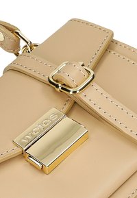 Beige leren handtas met een gladde textuur, voorzien van gouden hardware, een gespband en een gepolijste sluiting met branding.