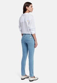 Jeans skinny azzurri con tasche posteriori, abbinati a una camicia bianca larga. La camicia presenta un piccolo dettaglio a stella gialla vicino al colletto.