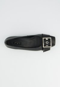 Chaussure plate en cuir noir avec un bout carré, ornée d'une grande boucle carrée métallique et d'une texture lisse. Logo intérieur imprimé.