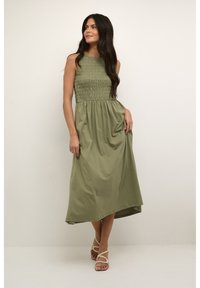 Rochie midi, fără mâneci, de culoare verde măslinie, cu un corp elastic, fustă fluidă și un tiv ușor asimetric. Purtați cu sandale cu barete.