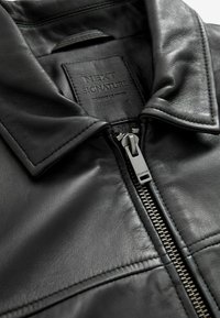 Schwarzlederjacke mit klassischem Kragen, Reißverschluss mit silberner Hardware und strukturiertem Obermaterial mit subtilen Nähdetails.