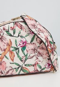 Sac à main matelassé au motif floral dans des teintes de rose, orange et vert. Pr�ésente des garnitures en or et le nom de la marque "GUESS" embossé en argent.