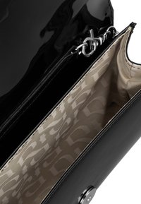 Czarna torebka z lakierowanej skóry z zapięciem z srebrnym okuciem, w beżowym wnętrzu z powtarzającym się wzorem logo.