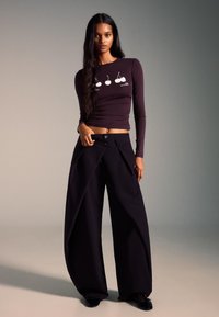 Tričko s dlhým rukávom tmavofialovej farby s bielou grafikou čerešní; kombinované s veľkými čiernymi plisovanými nohavicami so zapínaním na dva gombíky.