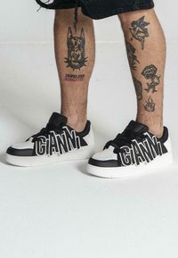 Crne i bijele tenisice s istaknutim "GIANNI" logotipom, izrađene od glatke kože s kontrastnim naglascima i teksturiranom potplatom.
