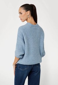 Maglione azzurro chiaro lavorato a maglia con una trama a coste, maniche a tre quarti e scollo rotondo, abbinato a jeans blu scuro.