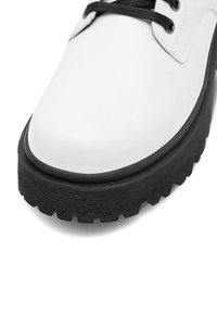 Baltas ādas apavs ar noapaļotu purngalu, melnu biezu gumijas zoli ar reljefa tekstūru un melnas auklas. Minimālisma dizains bez rotājumiem.