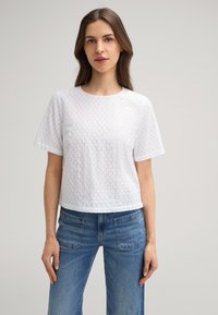 Witte katoenen t-shirt met een gestructureerd patroon, korte mouwen en een ronde hals. Gecombineerd met blauwe jeans voor een casual look.