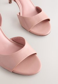 Sandales à talons roses en matériau synthétique lisse, avec une large bride sur le dessus, un design à bout ouvert et un talon effilé.