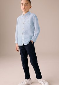 Lyseblå skjorte med knapper og brystlomme, kombineret med marineblå bukser og hvide sneakers. Glat stof, afslappet pasform, lange ærmer.