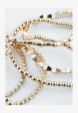 Goudvergulde metalen armbanden in verschillende vormen, waaronder rond en hexagonaal. Ze hebben afwisselend textuurrijke en gladde oppervlakken met verschillende kralenstijlen.