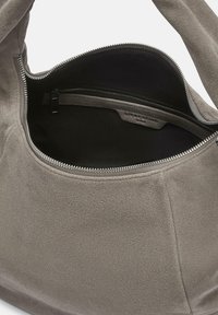 Szara torebka z zamszu z główną komorą na zamek błyskawiczny, wyposażona w miękką podszewkę wewnętrzną oraz dodatkową kieszonkę na zamek. Gładka tekstura.