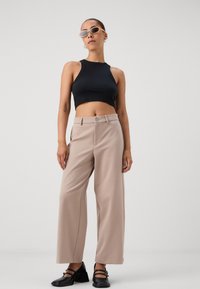 Svart kortärmad crop-top, beige vida byxor med knappstängning och svarta klackskor. Minimalistisk design och släta texturer.