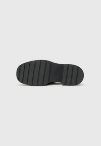 Suola di scarpa in gomma nera con una superficie testurizzata e scanalature orizzontali per una migliore aderenza. Testo del logo visibile nel design.