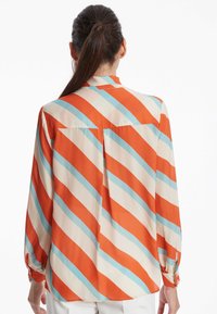 Langärmlige, knöpfbare Bluse mit vertikalen Streifen in Orange, Blau und Creme. Weicher Stoff mit lockerer Passform und einem Rückenfalte.
