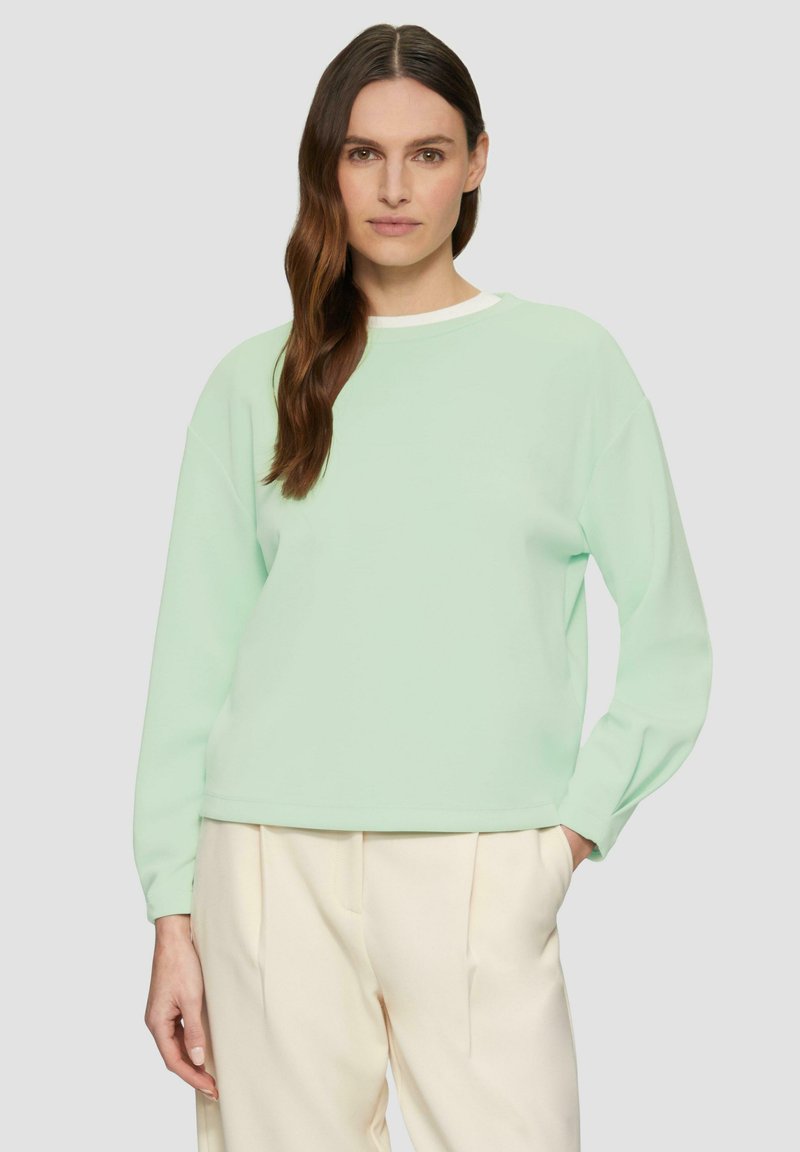 Mintgroene sweatshirt met een relaxte pasvorm, ronde halslijn en lange mouwen, met een zachte stof en een eenvoudig ontwerp. Gepaard met beige broeken.
