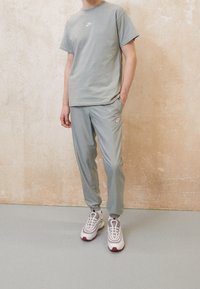 Ljust grå Nike t-shirt och matchande byxor, båda i avslappnad passform. Vitt Nike-logotyp på bröstet och byxorna. Vita och grå sneakers med röda detaljer.