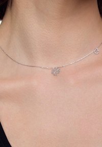 Srebrny naszyjnik z delikatnym łańcuszkiem, zdobiony kwiatowym wisiorkiem, o skomplikowanym wzorze i małych akcentach po obu stronach.