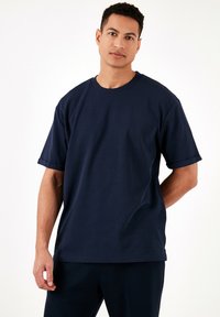 Tricou din bumbac de culoare bleumarin, cu un croi lejer, mâneci scurte și guler rotund; prezintă un model texturat pe țesătură.