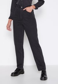 Högmidjade, raka mörkgrå jeans med bälteshällor och framfickor, i kombination med svarta snörskor på en enfärgad bakgrund.