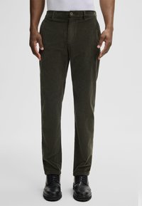 Olijfgroene corduroy broek met een rechte snit, voorzien van een knoopsluiting, zijzakken en gedragen met zwarte laarzen.