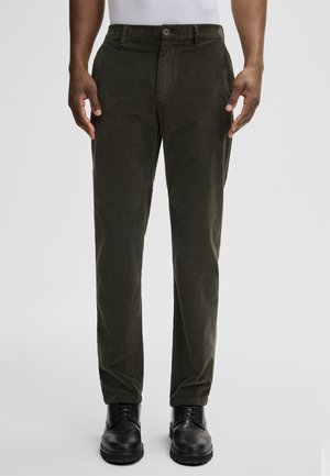 Olijfgroene corduroy broek met een rechte snit, voorzien van een knoopsluiting, zijzakken en gedragen met zwarte laarzen.
