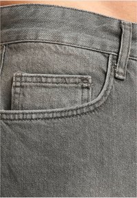 Jeans de mezclilla gris con un pequeño bolsillo trasero, una textura suave y un diseño elegante con costuras en contraste a lo largo de los bordes.
