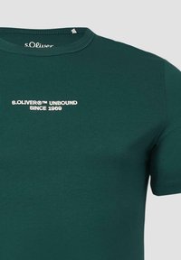 Zielona bawełniana koszulka z krótkim rękawem, z okrągłym dekoltem. Na przodzie czarny napis "s.Oliver™ UNBOUND SINCE 1969".