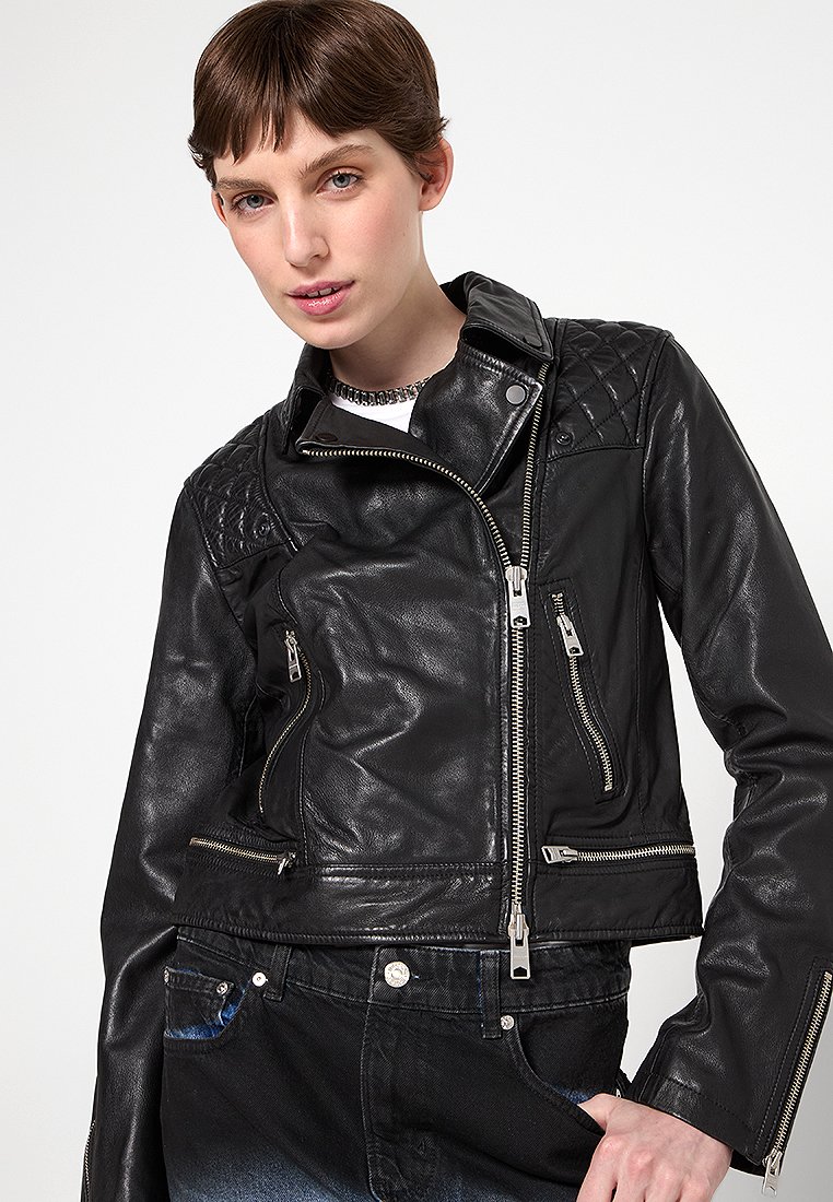 Giacca da moto in pelle nera con tasche con zip, design delle spalle trapuntato e accenti in metallo argentato. Texture liscia e forma aderente.