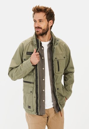 Olive green, multi-pocket jacket with a zip closure, snap buttons, and a textured finish. Features a layered design over a gray shirt.