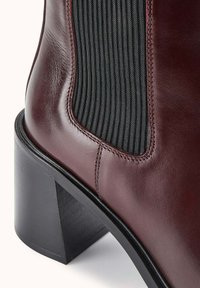 Botte en cuir bordeaux foncé avec panneau latéral élastique noir et talon bloc noir épais, gros plan sur les détails de la tige et du talon.